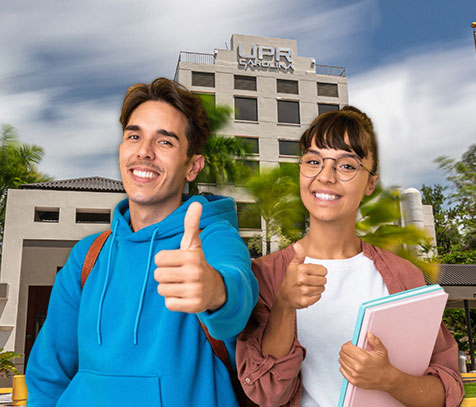 Foto de dos estudiantes sonriendo frente al edificio principal de la UPR en Carolina.
